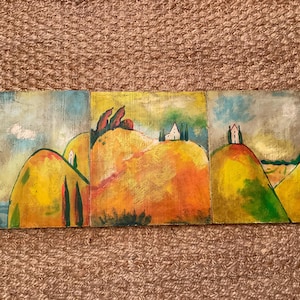 May include: A triptych painting depicting rolling hills in shades of yellow, orange, and green under a cloudy sky. Small white houses are perched atop the hills, with tall, thin trees adding vertical accents. The artwork has a rustic, textured appearance.