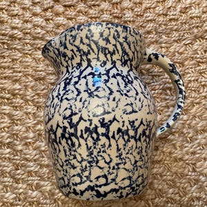 以下が含まれることがあります： クリーム色のベースに青い飛沫模様が施されたセラミックピッチャー。ピッチャーには、曲がったハンドルと注ぎ口が付いています。デザインはヴィンテージの農家風の装飾を彷彿とさせます。ピッチャーは飲み物の提供に適しています。