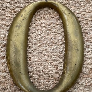May include: A large, vintage-style letter "O" in a metallic gold finish. The decorative numeral has a slightly distressed appearance, with visible wear and tear, suggesting an antique or reclaimed aesthetic. The letter is likely used for home decor or signage.