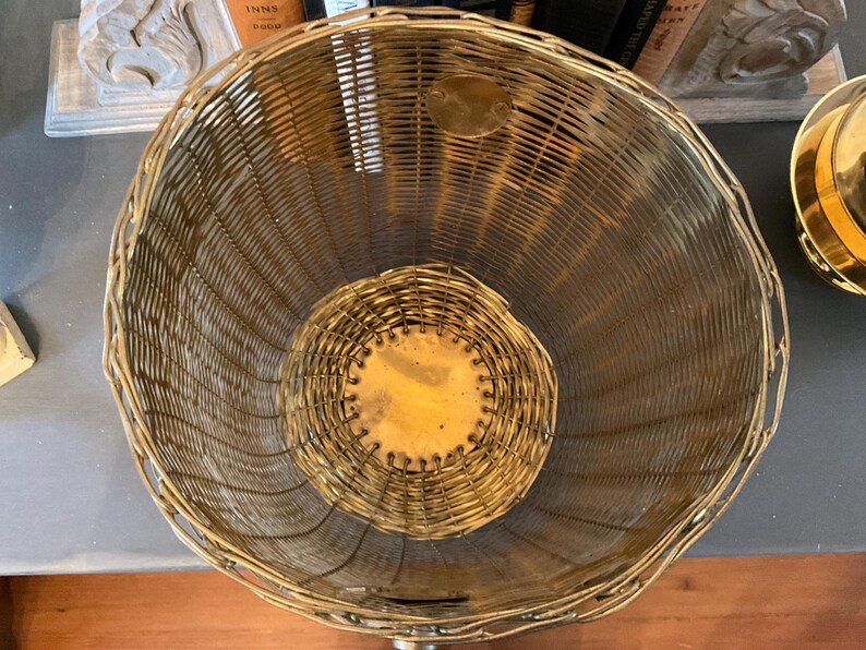 May include: A vintage, open-weave basket with a rounded shape. The basket is made of gold-toned metal wire, with a circular base and a slightly flared top. The interior features a smaller, circular base. The basket is likely used for storage or display.