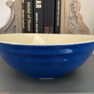 Könnte beinhalten: Eine große, vintage Keramikschüssel mit glänzend kobaltblauer Außenseite und cremefarbenem Innenraum. Die Schüssel hat eine breite, flache Form und einen leicht abgenutzten Rand. Die Schüssel ist wahrscheinlich zum Servieren oder Mischen geeignet, ca. 30 cm Durchmesser.