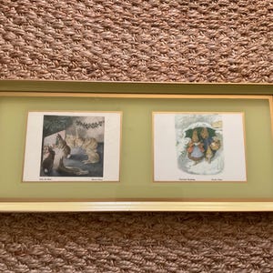 Könnte beinhalten: Ein gerahmtes Kunstwerk mit zwei Illustrationen. Das linke Bild zeigt Kaninchen in der Nähe eines Gartens, und das rechte zeigt Kaninchen unter einem Regenschirm im Schnee. Der Rahmen ist hellgrün mit goldenem Rand.