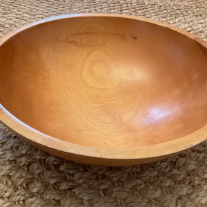 May include: A large, oval wooden bowl with a light brown finish. The bowl has a smooth, polished interior and a slightly textured exterior. The wood grain is visible throughout the bowl. This decorative bowl is suitable for serving salads or displaying fruit.