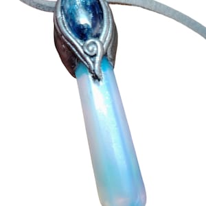 May include: A pendant necklace with an iridescent, light blue and white crystal pendant. The pendant is attached to a grey suede cord. The top of the pendant has a silver-coloured metal setting with a blue stone.