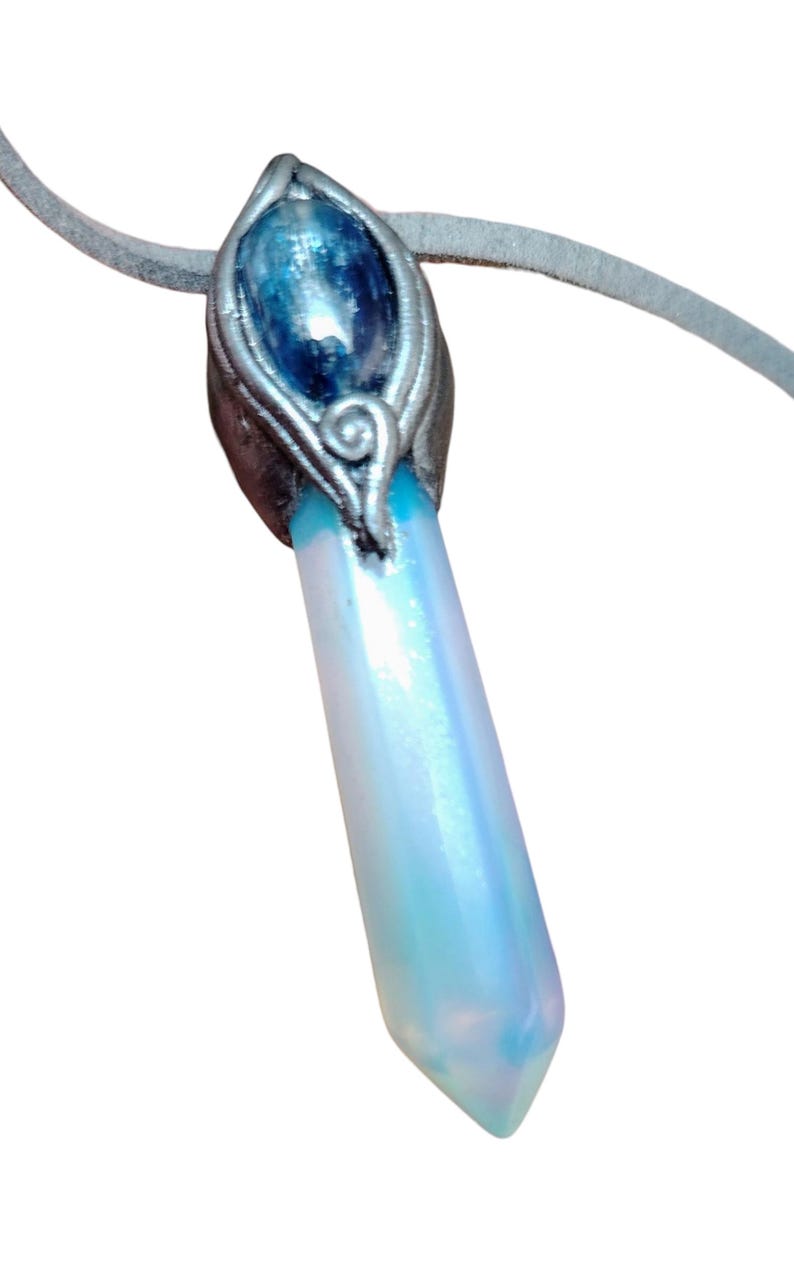 May include: A pendant necklace with an iridescent, light blue and white crystal pendant. The pendant is attached to a grey suede cord. The top of the pendant has a silver-coloured metal setting with a blue stone.