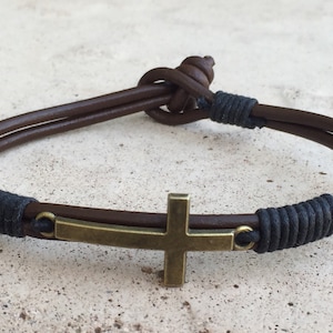 May include: A brown leather bracelet with a black cord and a metal cross charm.
