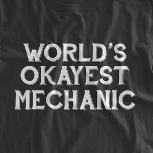 May include: Black t-shirt with white text that reads "WORLD'S OKAYEST MECHANIC".