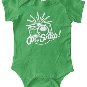 May include: A green baby onesie with a white graphic of a camera with a flash and the text "Oh Snap!"