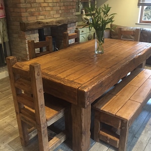 May include: A rustic wooden dining table with matching chairs and a bench. The table is rectangular, with a natural wood finish and visible grain. A clear glass vase with green stems sits on the table. The chairs and bench have a similar design.