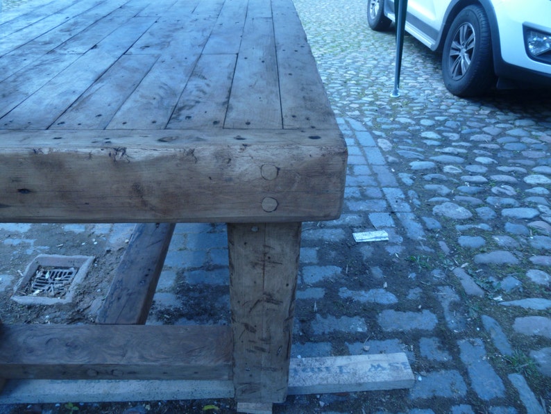 May include: A large, rustic wooden table with a thick, weathered top and sturdy legs. The table is made of reclaimed wood and has a natural, distressed finish.
