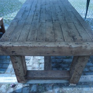 May include: A rustic wooden table with a thick, weathered top and sturdy legs. The table is made of reclaimed wood and has a natural, distressed finish.