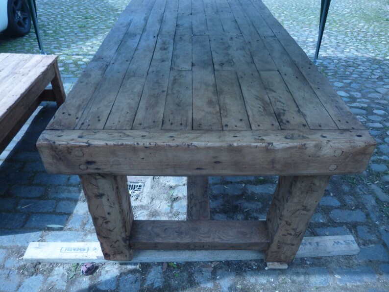 May include: A rustic wooden table with a thick, weathered top and sturdy legs. The table is made of reclaimed wood and has a natural, distressed finish.