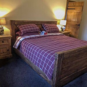 May include: A wooden bed frame with a purple and white checked duvet and pillows. The bed is in a bedroom with a wooden door and a bedside table.