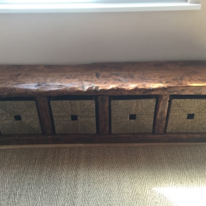 May include: A rustic wooden bench with four woven baskets underneath. The bench has a natural wood finish and the baskets are a light brown color.