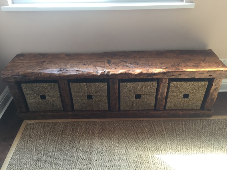 May include: A rustic wooden bench with four woven baskets underneath. The bench has a natural wood finish and the baskets are a light brown color.