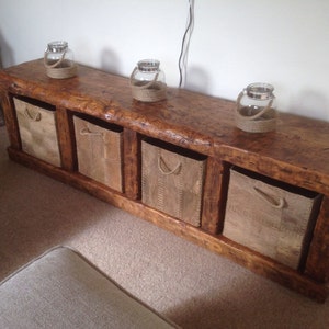 May include: A rustic wooden bench with four storage bins and a natural wood finish. The bench has a distressed look and is decorated with three glass jars with twine handles.