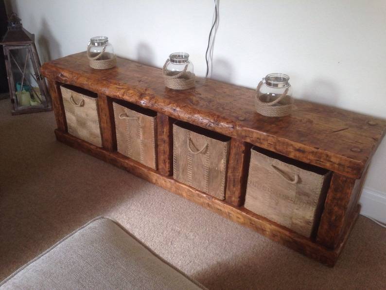 May include: A rustic wooden bench with four storage bins and a natural wood finish. The bench has a distressed look and is decorated with three glass jars with twine handles.