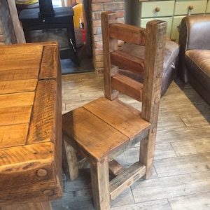 May include: A rustic wooden chair with a slatted back and seat, constructed from reclaimed wood. The chair has a square seat and sturdy legs, showcasing the natural grain and knots of the wood. The chair is part of a dining set.