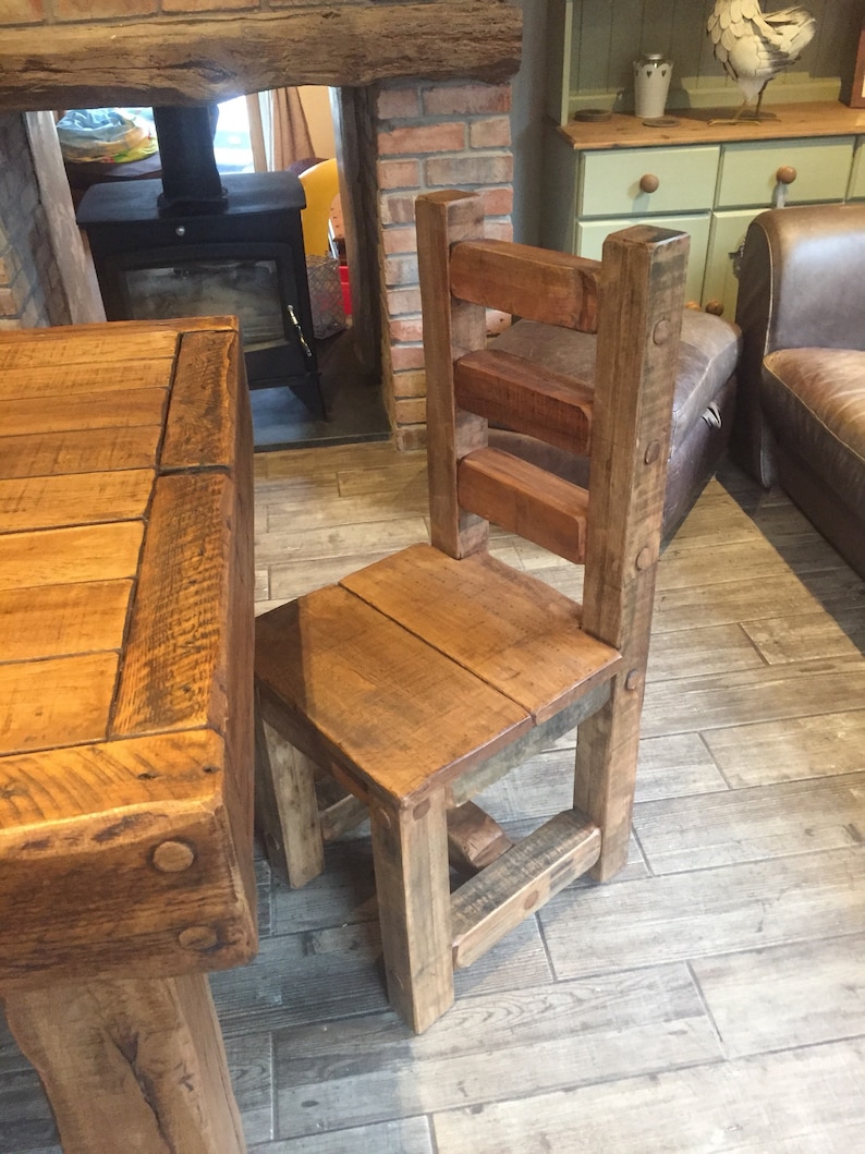 May include: A rustic wooden chair with a slatted back and seat, constructed from reclaimed wood. The chair has a square seat and sturdy legs, showcasing the natural grain and knots of the wood. The chair is part of a dining set.