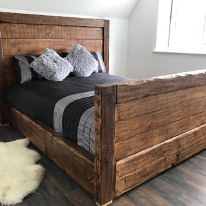 May include: A rustic wooden bed frame with a high headboard and a thick, dark brown finish. The bed is made of reclaimed wood and has a simple, elegant design.
