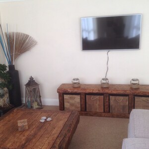 May include: A rustic wooden TV stand with four storage bins, a flat screen TV mounted on the wall above, and a wooden coffee table with three decorative stones on top.