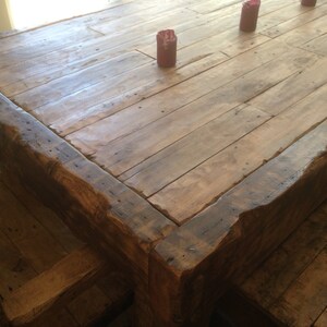 May include: A rustic wooden dining table with a thick, uneven top and a natural wood finish. The table has a rough-hewn edge and is made of reclaimed wood planks.