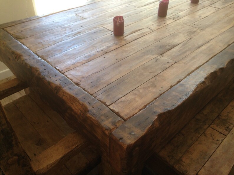 May include: A rustic wooden dining table with a thick, uneven top and a natural wood finish. The table has a rough-hewn edge and is made of reclaimed wood planks.