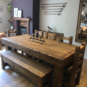 May include: A rustic wooden dining table with a bench and chairs. The table is made of reclaimed wood and has a natural finish. The bench and chairs are also made of wood and have a similar finish. The table is set with a candle holder and candles.