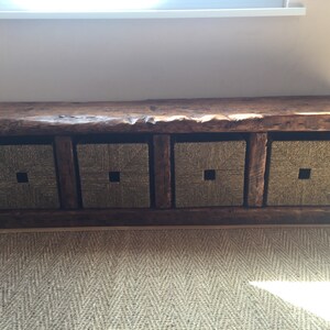 May include: A rustic wooden bench with four woven storage baskets. The bench has a natural wood finish and the baskets are a light brown color.