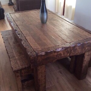 May include: A rustic wooden dining table with a thick, weathered top and a matching bench. The table has a dark brown stain and is made of reclaimed wood. The bench is also made of reclaimed wood and has a natural finish.