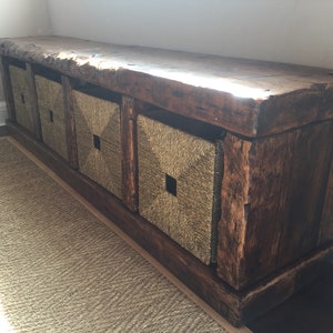 May include: A rustic wooden bench with four woven storage baskets. The bench is made of dark brown wood with a natural finish. The baskets are made of natural woven material and have a square shape.