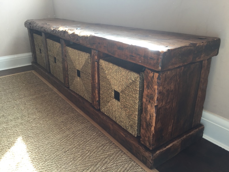 May include: A rustic wooden bench with four woven storage baskets. The bench is made of dark brown wood with a natural finish. The baskets are made of natural woven material and have a square shape.