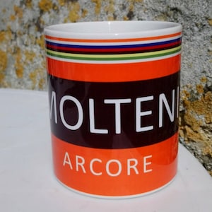 May include: A white ceramic mug with a red, black, and white design. The mug has the words "MOLTENI ARCORE" printed on it.