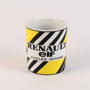以下が含まれることがあります： 黄色と黒のストライプのセラミックマグカップで、"Renault elf CYCLES GITANE"の文字が印刷されています。