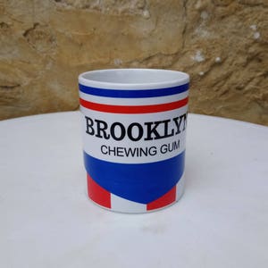 May include: White ceramic mug with a blue, red, and white design. The mug has the text "BROOKLYN CHEWING GUM" printed on it.