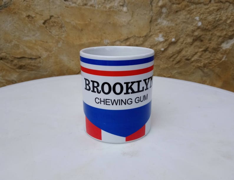 May include: White ceramic mug with a blue, red, and white design. The mug has the text "BROOKLYN CHEWING GUM" printed on it.