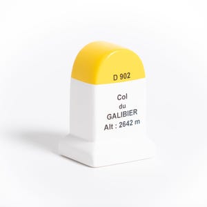 Puede incluir: Un marcador decorativo blanco y amarillo con el texto "D 902" y "Col du GALIBIER Alt: 2642 m". El marcador tiene una base rectangular y una parte superior redondeada. La altitud es de 2642 metros.