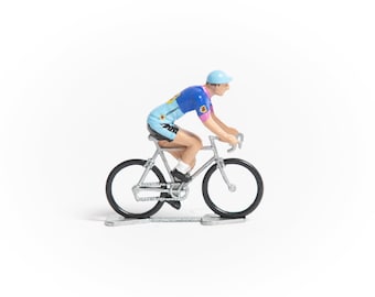 Può includere: Una figurina da ciclismo blu e rosa che guida una bicicletta argentata con pneumatici neri. La figurina indossa un casco blu e una maglia blu e rosa.