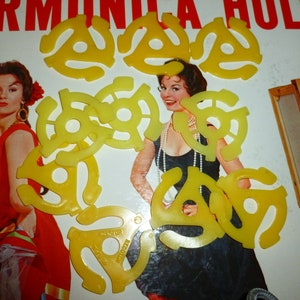 May include: A collection of ten yellow plastic 45 RPM record adapter spindle center holes. The adapters are arranged in a random pattern on a white surface.