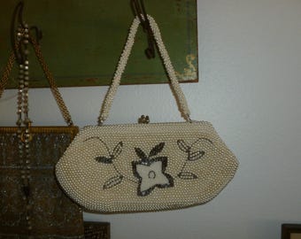 May include: A white beaded evening bag with a floral design. The bag has a silver clasp and a chain strap.