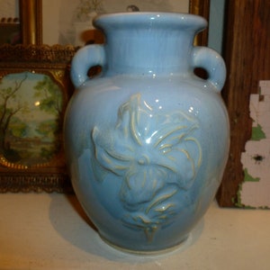 May include: A light blue ceramic vase with a raised floral design. The vase has two handles and a rounded body.