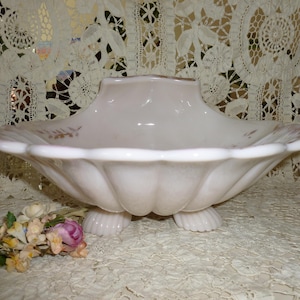 May include: A white, footed, scalloped bowl with a delicate floral design. The bowl is made of milk glass and has a vintage look.