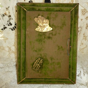 May include: A green velvet photo frame with a gold embossed design and a metal latch. The frame has a gold embossed image of two women in hats.