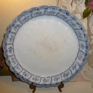 May include: A large, white ceramic serving platter with a blue and white floral pattern. The platter has a scalloped edge and is on a stand.