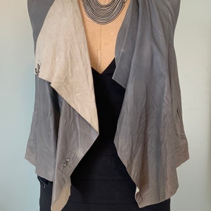 Puede incluir: Un chaleco de cuero gris con un diseño drapeado y un collar plateado con detalles turquesa.