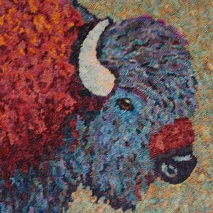 May include: Close-up of a colorful rug depicting a bison with a white horn. The bison's fur is a mix of blue, purple, and red, with a brown nose and a red muzzle.