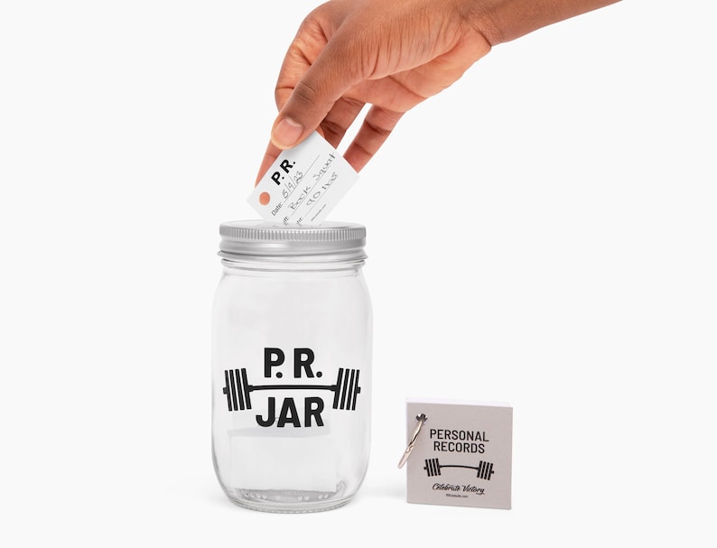 PR Jar™ for Personal Records, Weightlifting, Powerlifting, Crossfit. Jar is clear. Design is black. Coin slot lid is silver. Notepad included. The PR Jar™ is an original FitFizz creation that makes an excellent gift for yourself or any lifter.