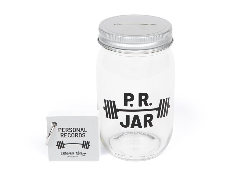 PR Jar™ for Personal Records, Weightlifting, Powerlifting, Crossfit. Jar is clear. Design is black. Coin slot lid is silver. Notepad included. The PR Jar™ is an original FitFizz creation that makes an excellent gift for yourself or any lifter.