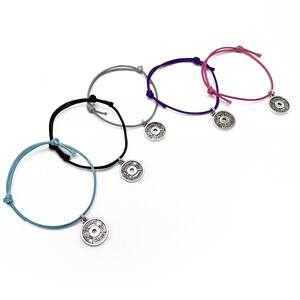 May include: Four colorful string bracelets with silver weight plate charms. The bracelets are in blue, black, gray, and pink.