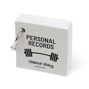 Close-up of the front of the notepad. The cover is silver paper that says Personal Records with a barbell underneath. Bound with a silver ring.